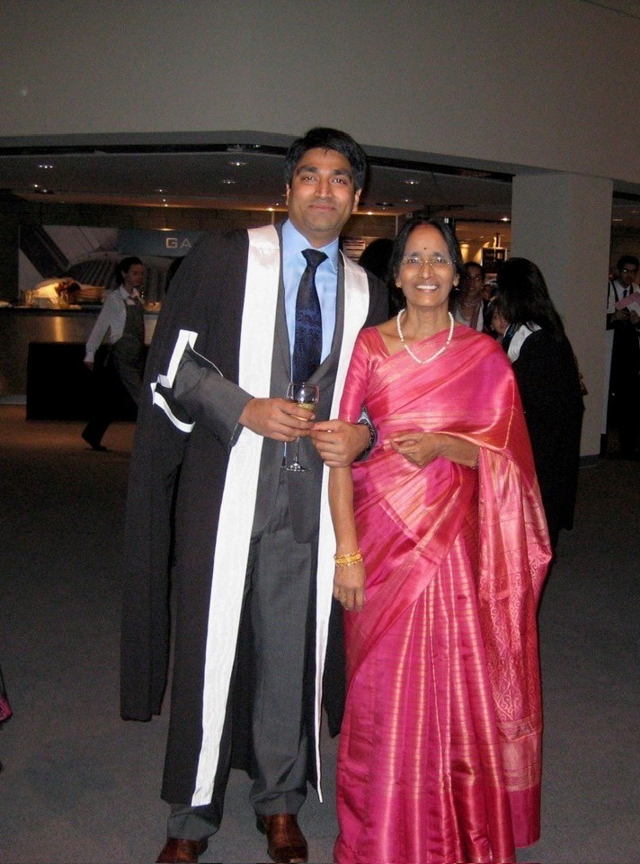 Dr Che Tadi in academic robes on graduation day, with his mother in a pink saree